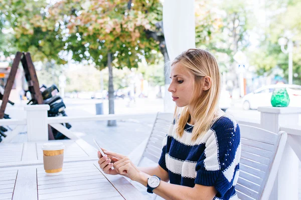 Eine junge Frau schickt im Café eine SMS von ihrem Handy. Frau benutzt Smartphone auf Holztisch in Outdoor-Café — Stockfoto