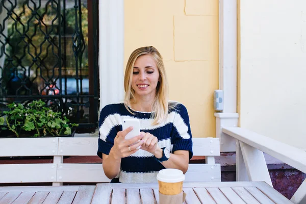 Młoda kobieta wysyła SMS-a z komórki w kawiarni. Kobieta korzystająca ze smartfona na drewnianym stole w kawiarni na świeżym powietrzu — Zdjęcie stockowe