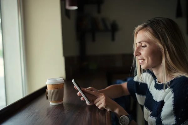 Eine junge Frau schickt im Café eine SMS von ihrem Handy. Frau benutzt Smartphone auf dem Holztisch — Stockfoto