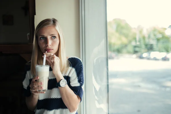 Porträtt av ung kvinna dricker kaffelatte i kaféet nära fönstret — Stockfoto