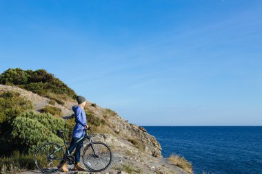 çekici genç gülümseyen bisiklet ile sarışın kadın bir kayada duran ve denize bakarak