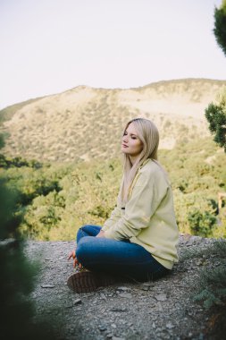 sarışın genç kadın mavi kot pantolon ve sarı dağlar bir arka plan üzerine açık oturma çalışma çizmeler