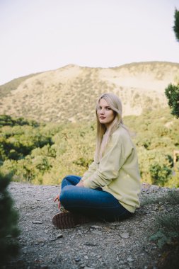 sarışın genç kadın mavi kot pantolon ve sarı dağlar bir arka plan üzerine açık oturma çalışma çizmeler