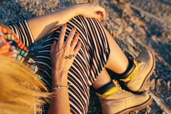 Imagen recortada de las manos de una mujer joven en un vestido a rayas, bufanda colorida y botas amarillas con el signo de clave de agudos imagen Mehndi. concepto — Foto de Stock