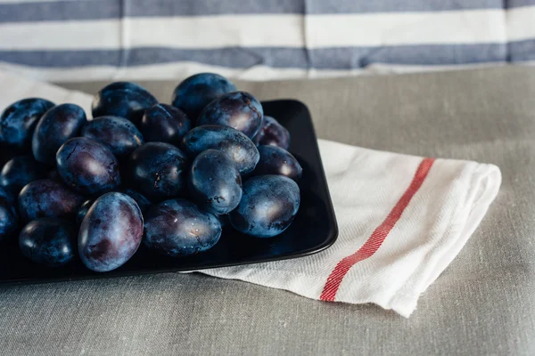 Ripe plums in a plate on a rural tablecloth and textile napkins — Stock Photo, Image