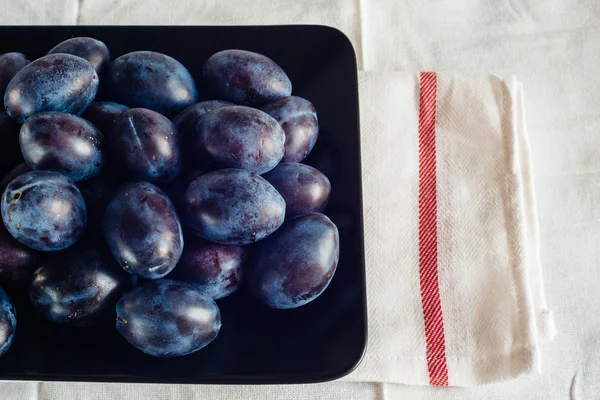Ripe plums in a plate on a rural tablecloth and textile napkins — Stock Photo, Image