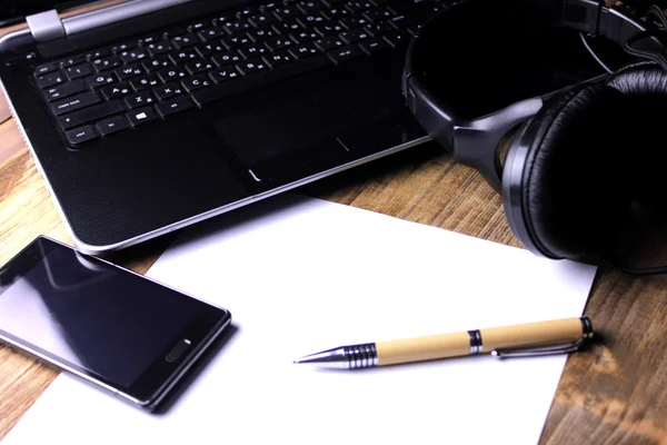 Smartphone, kulaklık ve bir ahşap masaüstü üstünde Laptop.