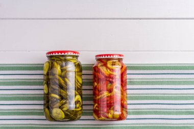 Çizgili kumaş üzerine salatalık turşusu ve biber dolu kavanozlar beyaz ahşap zemin.