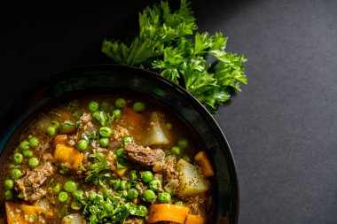 Sebzeli ve patatesli biftek yahnisi karanlık bir masada.