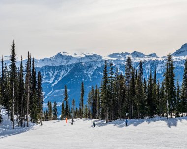 REVELSTOKE, Kanada - 17 Mart 2021: Kanada dağlarındaki yamaçtan kayakçılar ve snowboardcular