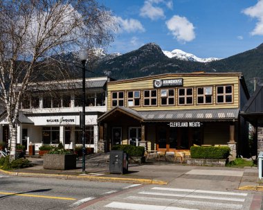 SQUAMISH, CANADA - 13 Nisan 2025: Dağlık mavi gökyüzünde küçük bir kasabada şehir yolları ve binalar