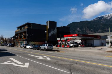 SQUAMISH, CANADA - 13 Nisan 2025: Dağlık mavi gökyüzünde küçük bir kasabada şehir yolları ve binalar