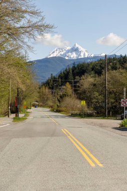 SQUAMISH, CANADA - 13 Nisan 2025: Dağlık mavi gökyüzünde küçük bir kasabada şehir yolları ve binalar
