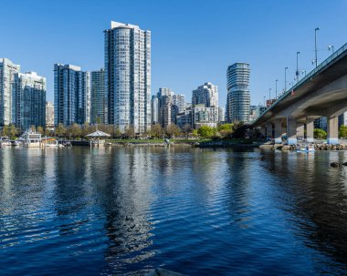 VANCOUVER, CANADA - 18 Nisan 2025: Modern yüksek binalar ve False Creek 'te parlak bir gökyüzü altında seyreden bir tekne ile şehir silueti