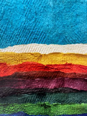 Colorful layered paper texture in vivid shades of blue, yellow, red, purple, green, and brown. Abstract handmade background with torn edges and rough surface, creative craft art design.
