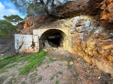 Çökmüş kayalar ve beton kemerle terk edilmiş bir yeraltı maden girişi. Kayalık yamaçtaki karanlık tünel, endüstriyel bozulma, tehlike ve gizem konsepti, keşif, jeoloji, tarih ve yıkım..