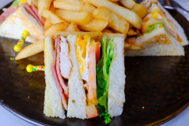 Club Sandwich 'in yakın plan çekimleri ve patates kızartması. Batı mutfağı. Öğle yemeği ve akşam yemeği. Yiyecek ve içecek konsepti.