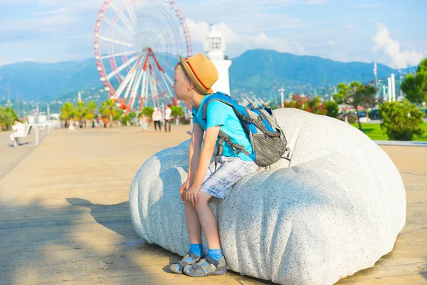 Boy with hat and  backpack  sitting on bench — Stock Photo, Image