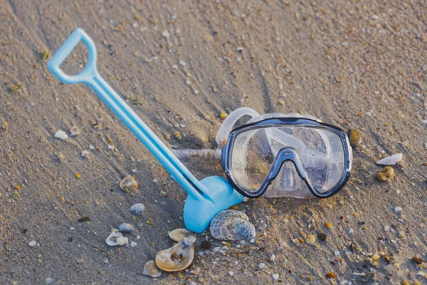 Summer vacation concept. Diving mask with shovel and shells on the sandy beach