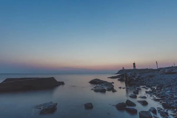 Leuchtturm an der Küste mit Steinen bei Sonnenuntergang — Stockfoto