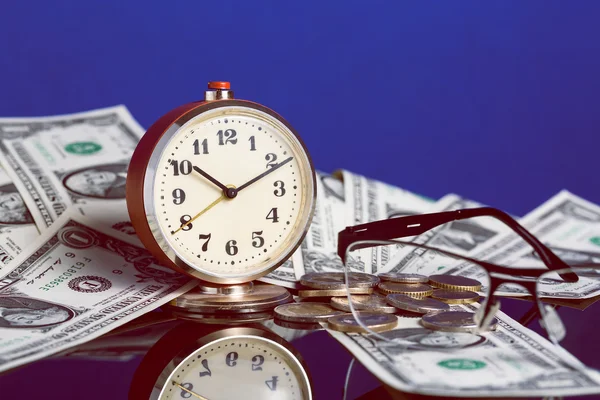 El tiempo es el concepto del dinero con el viejo reloj vintage, billetes de dólar, gafas y buena reflexión sobre el fondo azul —  Fotos de Stock