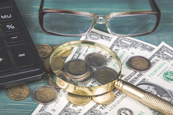 Concepto financiero. Calculadora, lupa, monedas de euro, penique británico, billetes de dólar y vasos en mesa de madera verde —  Fotos de Stock