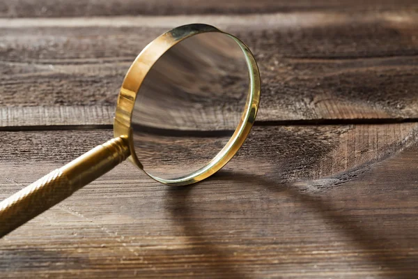 Gold magnifying glass with shadow on wooden background