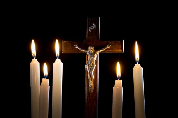 Crucifijo entre velas encendidas sobre fondo negro — Foto de Stock
