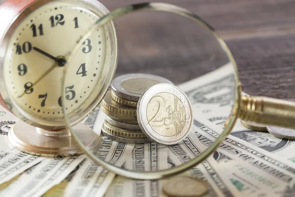 El tiempo es el concepto de finanzas monetarias con viejos relojes vintage, billetes de dólar, lupa y monedas de euro —  Fotos de Stock