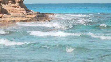 Tropikal dalgalar mavi bir yaz okyanusunun kayalık kıyılarına çarpıyor berrak bir gökyüzünün altında Agebah sahilinde güzel bir kumsal manzarası boyunca