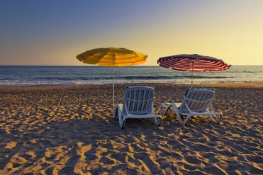 Yaz saati bir kumlu plajda güneş şemsiyeleri altında iki boş sandalye