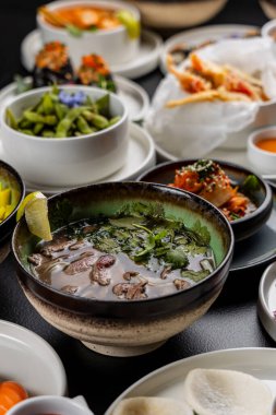 Asya mutfağıyla dolu büyük bir masa. Çorbalar, suşi, mezeler, dürtme kaseleri, karides, soslar.