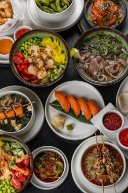 Asya mutfağıyla dolu büyük bir masa. Çorbalar, suşi, mezeler, dürtme kaseleri, karides, soslar.