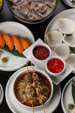 Asya mutfağıyla dolu büyük bir masa. Çorbalar, suşi, mezeler, dürtme kaseleri, karides, soslar.