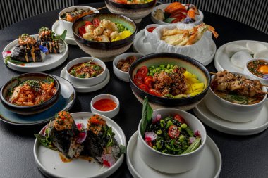 Asya mutfağıyla dolu büyük bir masa. Çorbalar, suşi, mezeler, dürtme kaseleri, karides, soslar.