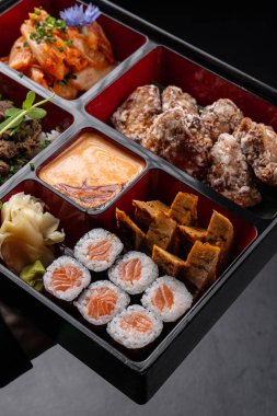 Suşi, kimchi, tofu, tempura ve soslu Japon usulü bento kutusu.