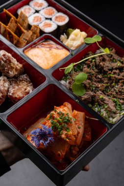 Suşi, kimchi, tofu, tempura ve soslu Japon usulü bento kutusu.