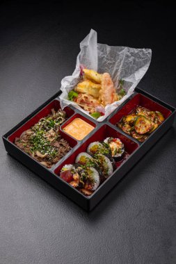 Japon stili bento kutusu, tempura ve suşi ile karanlık arka planda izole edilmiş.