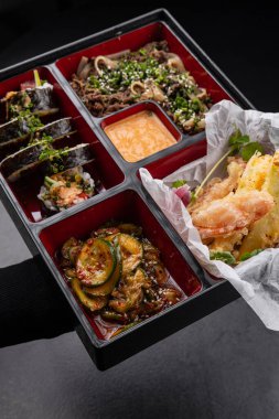 Japon stili bento kutusu, tempura ve suşi ile karanlık arka planda izole edilmiş.