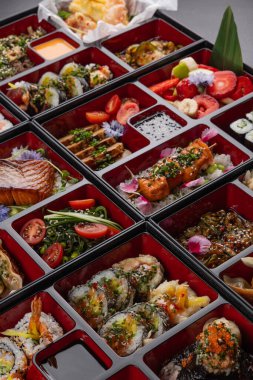 Japon mutfak yemekleriyle dolu kocaman bir bento kutusu. Suşi, saşimi, gyoza, tempura ve daha fazlası izole edilmiş karanlık bir arka planda.