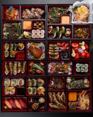 Japon mutfak yemekleriyle dolu kocaman bir bento kutusu. Suşi, saşimi, gyoza, tempura ve daha fazlası izole edilmiş karanlık bir arka planda.