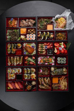 Japon mutfak yemekleriyle dolu kocaman bir bento kutusu. Suşi, saşimi, gyoza, tempura ve daha fazlası izole edilmiş karanlık bir arka planda.