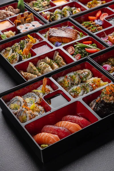 Japon mutfak yemekleriyle dolu kocaman bir bento kutusu. Suşi, saşimi, gyoza, tempura ve daha fazlası izole edilmiş karanlık bir arka planda.