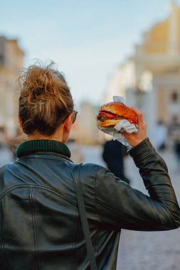 Yaşlı bir Avrupa şehrinin caddesinde genç bir kız onu yemeden önce bir burger tutuyor.