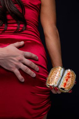 Kırmızı elbiseli baştan çıkarıcı kız elinde suşi burgeri tutuyor. Seksi yemek.