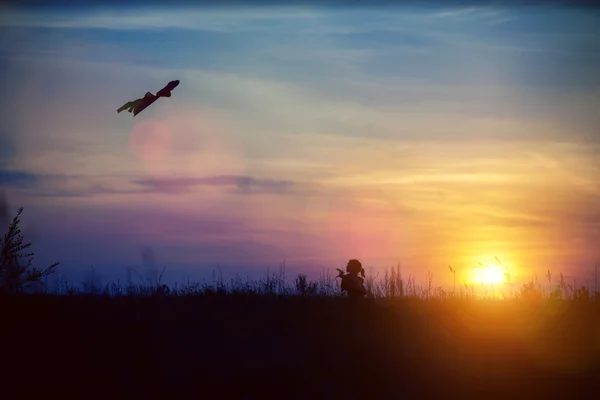 Fille et cerf-volant volant au coucher du soleil — Photo