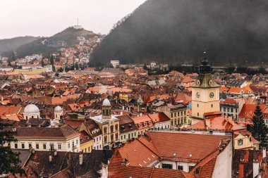 Romanya 'nın tarihi Brasov kentinin panoramik manzarası, karpatya dağlarında karamsar sis veya alçak bulutlarla kaplı. Eski şehrin ana meydanında ve ortaçağ binalarında saat kulesi olan meclis binaları..