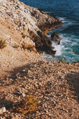 Arnavutluk 'un sakin kıyı manzarası ve kayalık uçurumlar arasında deniz körfezi. Sarp kayalıkları olan engebeli kıyı manzarası ve turkuaz Akdeniz suları ile küçük dalgalar kayalara çarpıyor..