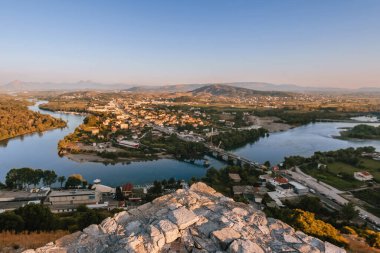 Arnavutluk 'un Şkoder kentindeki Rozafa Kalesi' nden panoramik manzara. Nehrin yüksek açılı görüntüsü, yemyeşil ağaçlar, yuvarlanan tepeler ve uzak dağlar. Tepedeki ortaçağ kalesinden manzara..