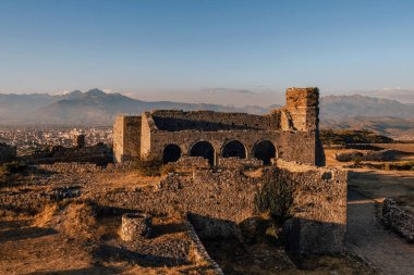 Gün batımında ya da gündoğumunda arkasında dağlar olan Rozafa Kalesi 'nin taş duvarları ve kemerleri. Ortaçağ kalesindeki St. Stephens Kilisesi 'nin tarihi kalıntıları. Arnavutluk 'un Şkodra kentinde popüler turizm simgesi.
